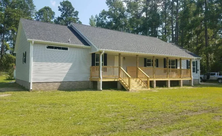 A newly built house with light gray siding, a dark gray roof, and a natural wood porch with railings.